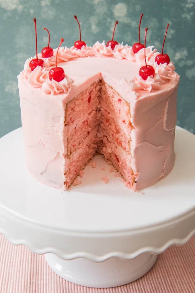 a vintage cherry chip cake on a white cake stand with a slice removed