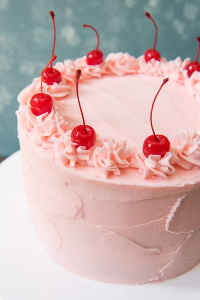 a pink frosted cake with cherries