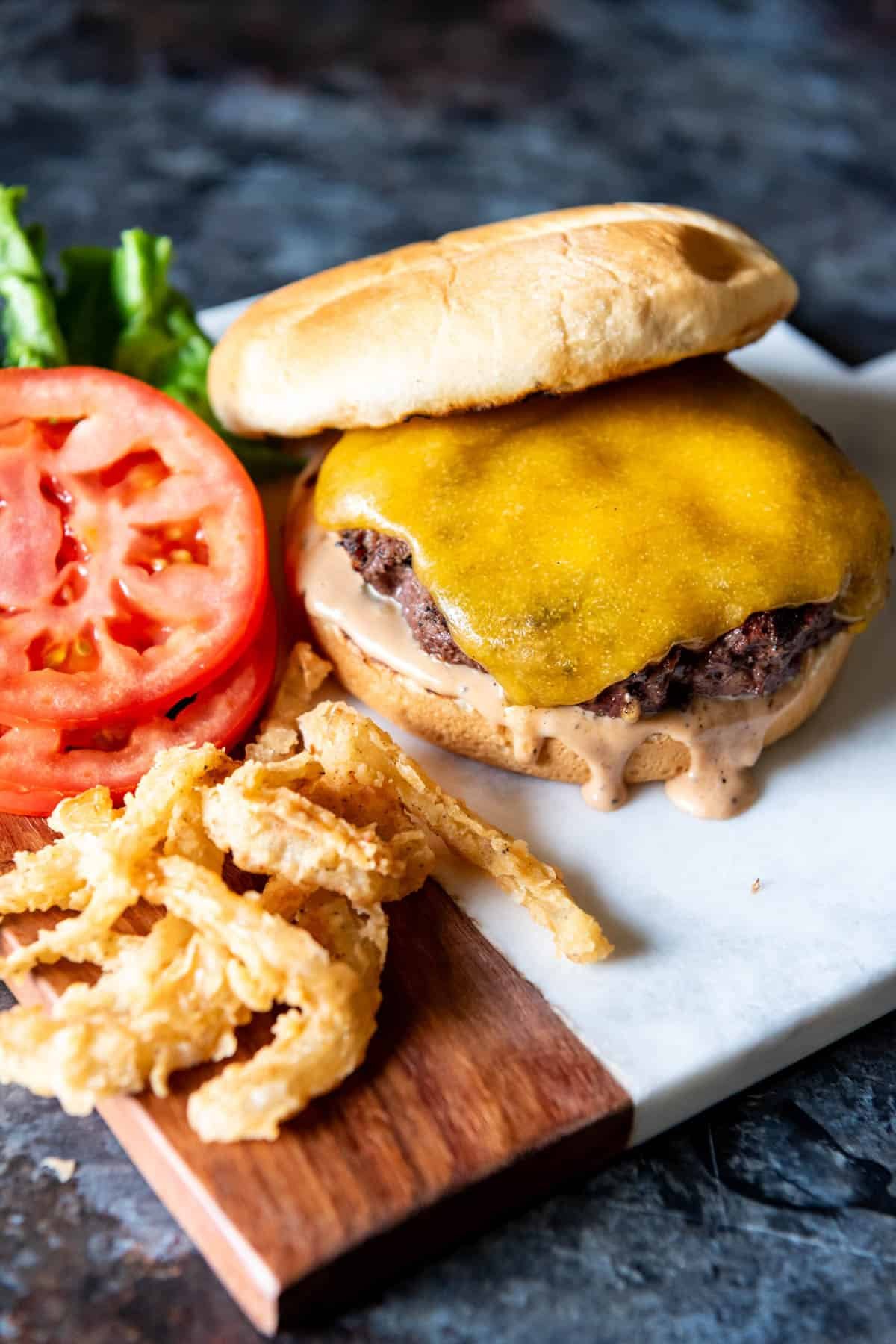 Cheeseburger with melted cheese next to sliced tomatoes and crispy onion strings.