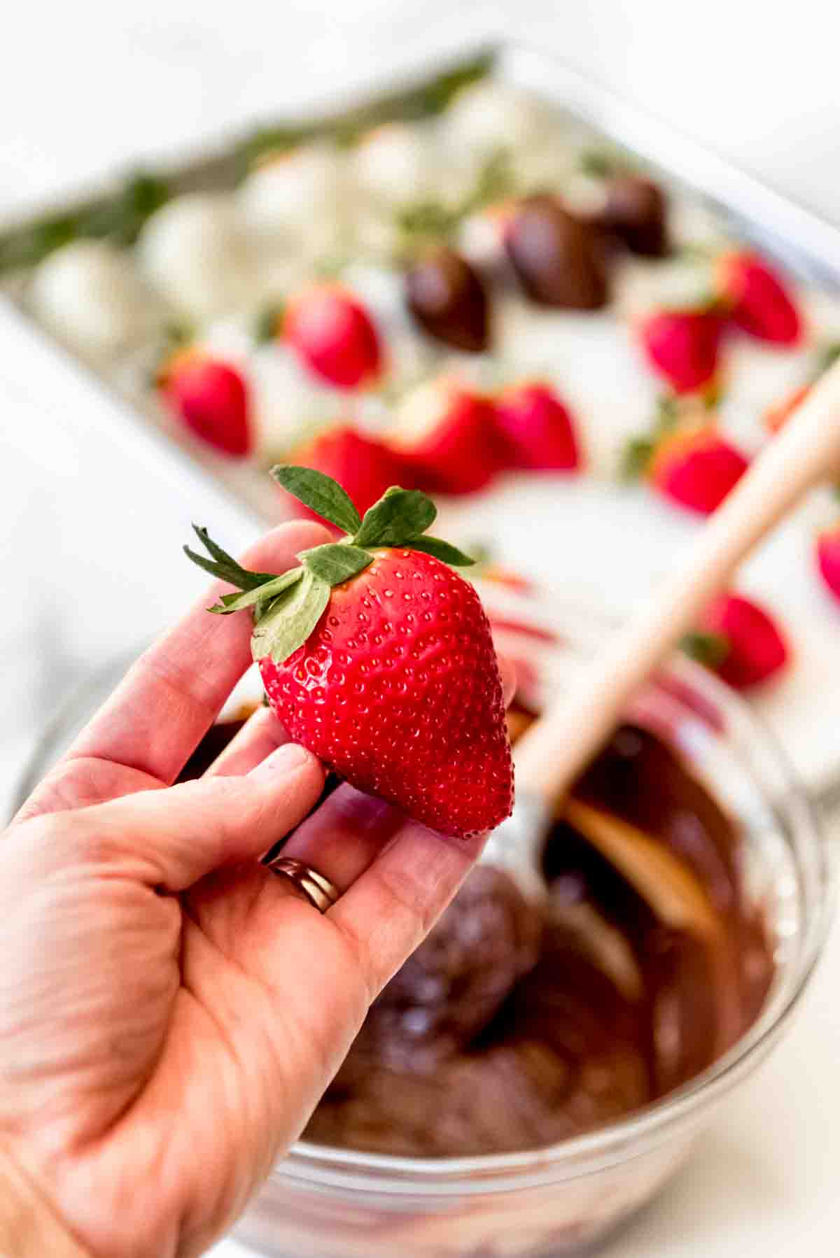 A hand holding a large fresh strawberry.