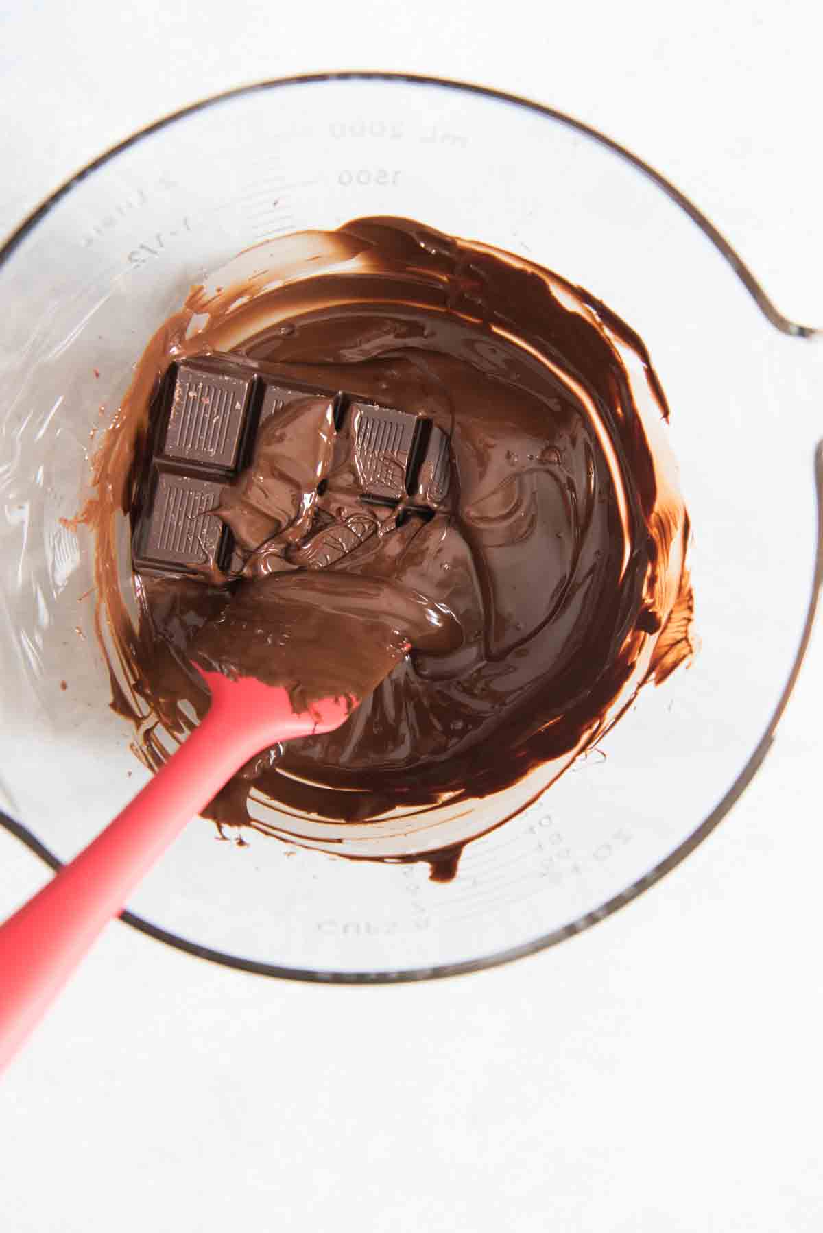 A bowl with melted chocolate and a chocolate bar and rubber spatula.