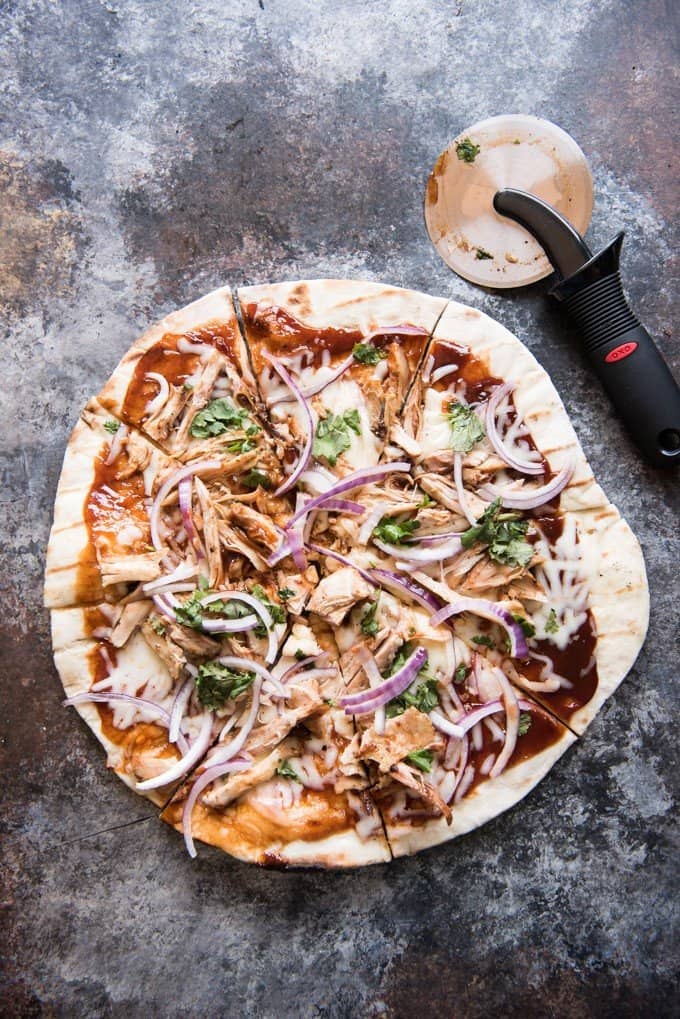 a sliced bbq chicken grilled pizza next to a rolling pizza cutter