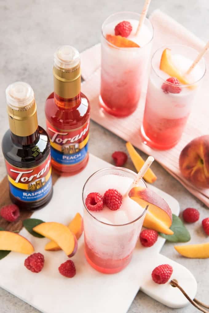 raspberry peach italian sodas with fresh fruit and torani syrup bottles in frame