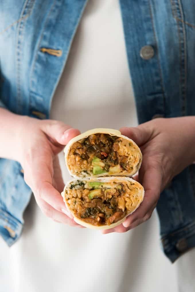 hands holding two halves of a vegetarian burrito to reveal the contents