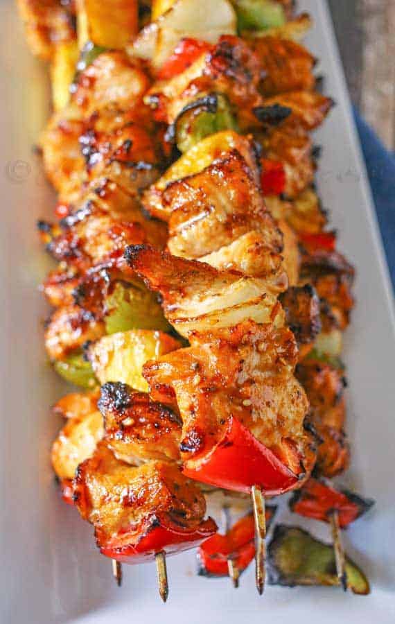 grilled chicken kabobs stacked on a white plate