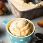 a scoop of peach ice cream in a blue and white polka dotted bowl in front of a tub of more ice cream