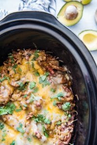 black slow cooker liner filled with melted cheese over flank steak brown rice casserole with an open avocado next to it