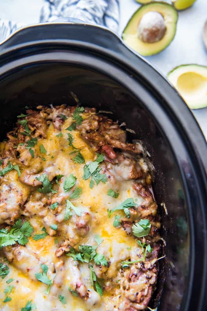 black slow cooker liner filled with melted cheese over flank steak brown rice casserole with an open avocado next to it