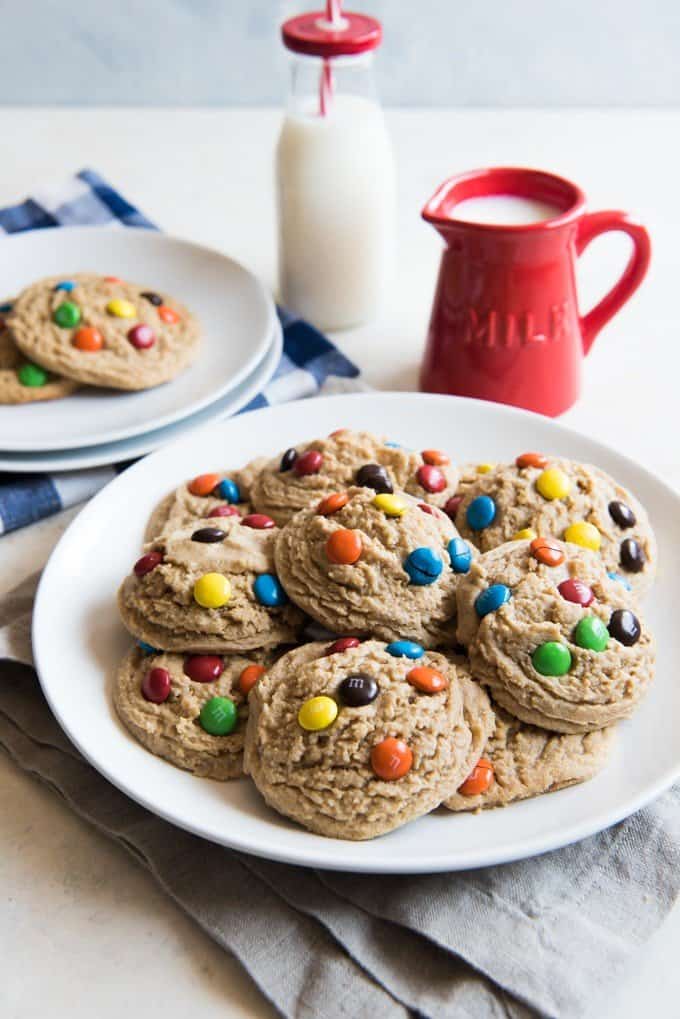a plate of M&M cookies with pitcher and bottle of milk in the background