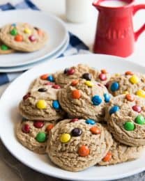 big and soft m&m cookies on ahwite plates with a pitcher of milk to the side