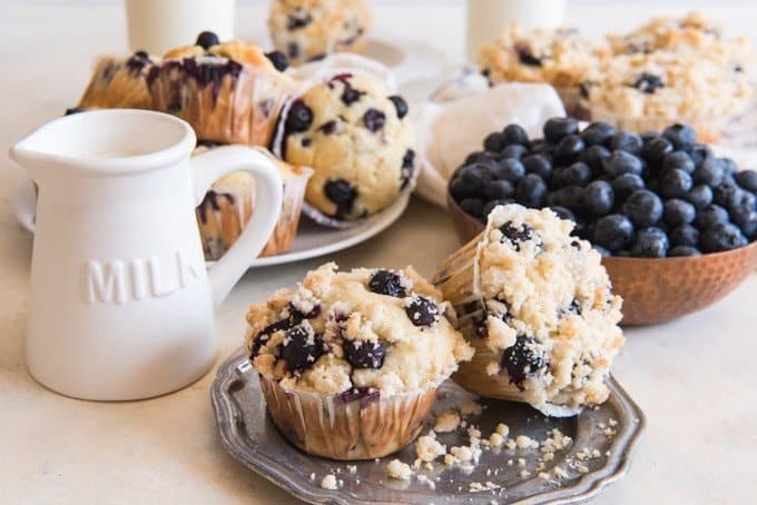 blueberry streusel muffins on plates with a bowl of blueberries to the side and a pitcher of milk on the other side