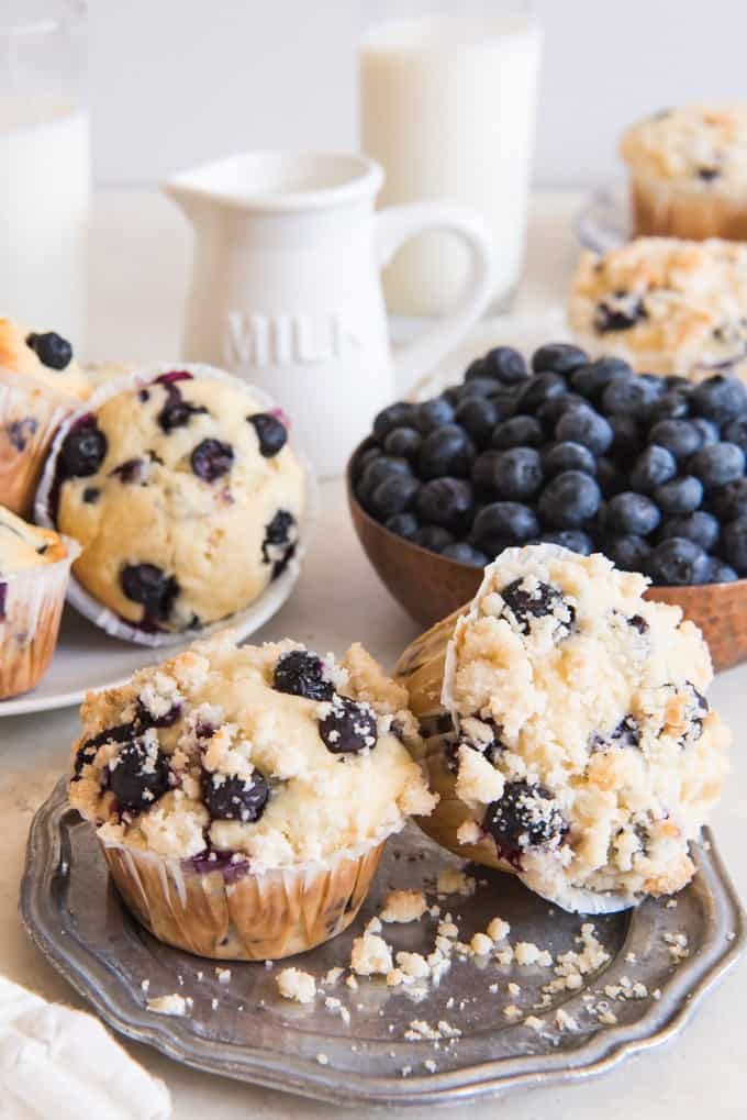 blueberry streusel muffins o plates with a bowl of fresh blueberries and milk in back