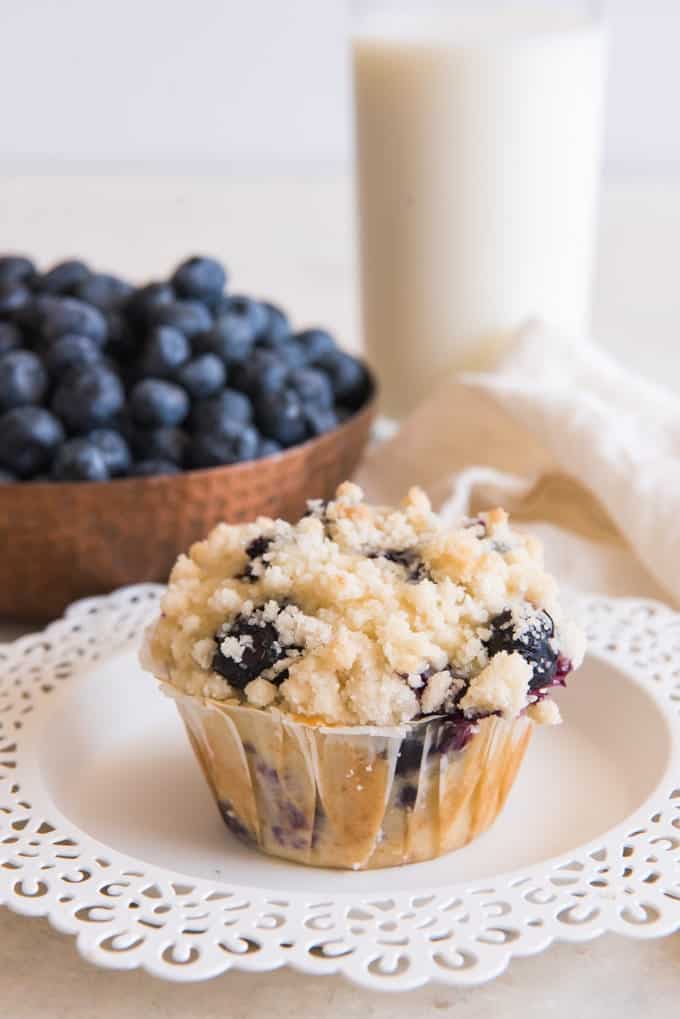 blueberry streusel muffin on a white plate with blueberries and milk in back