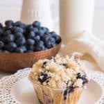 homemade blueberry muffin with streusel topping in front of pitcher of milk and bowl of fresh blueberries