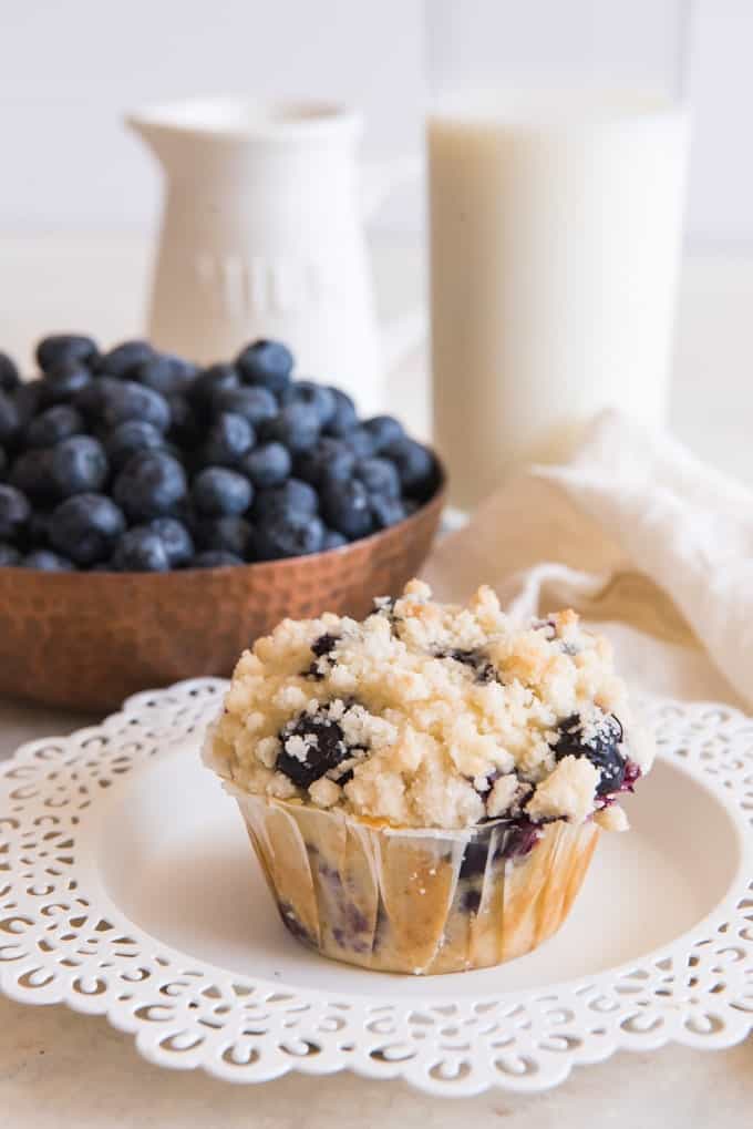 homemade blueberry muffin with streusel topping in front of pitcher of milk and bowl of fresh blueberries