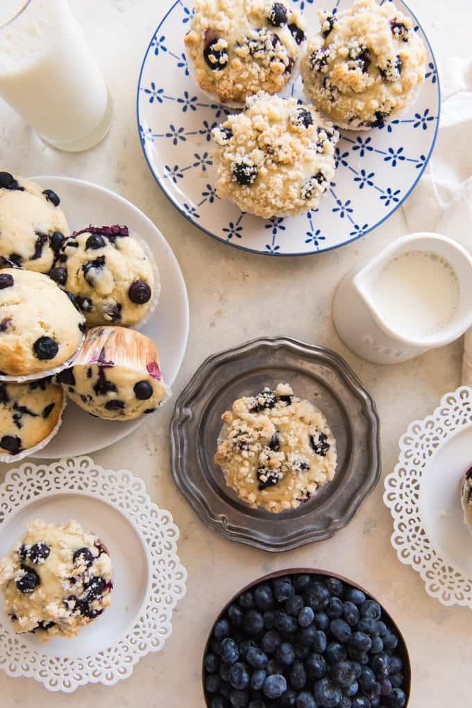blueberry streusel muffins on plates with a pile of no streusel muffins to the side