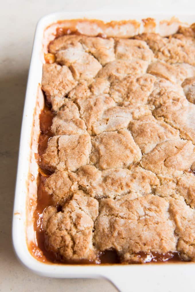 fresh peach cobbler in a baking dish with sauce around the top breading