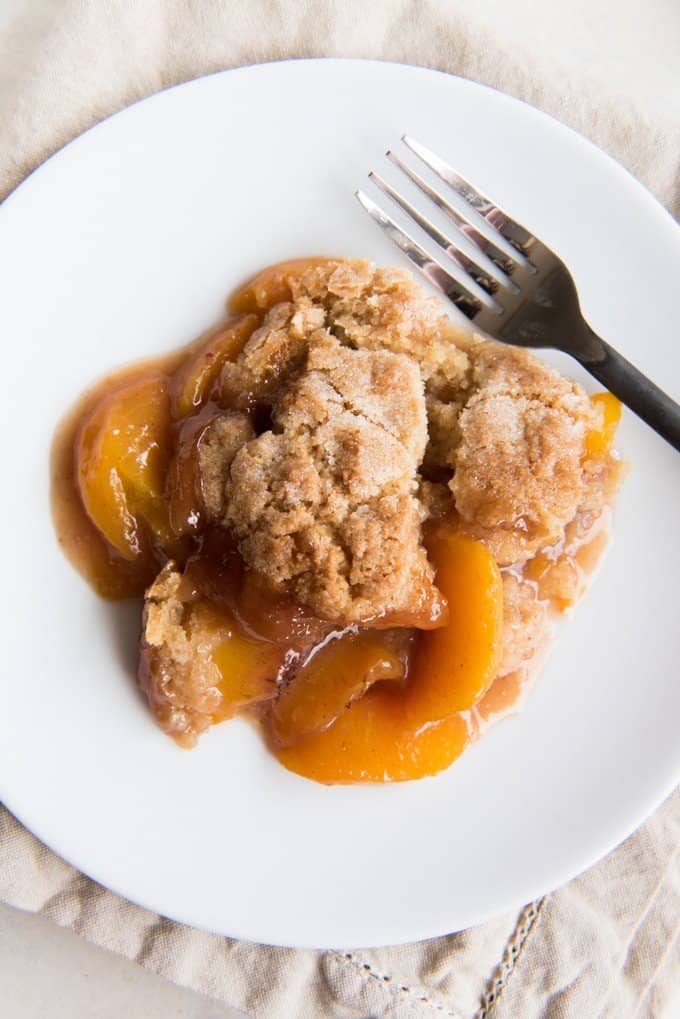 a white plate with fresh peach cobbler and a fork