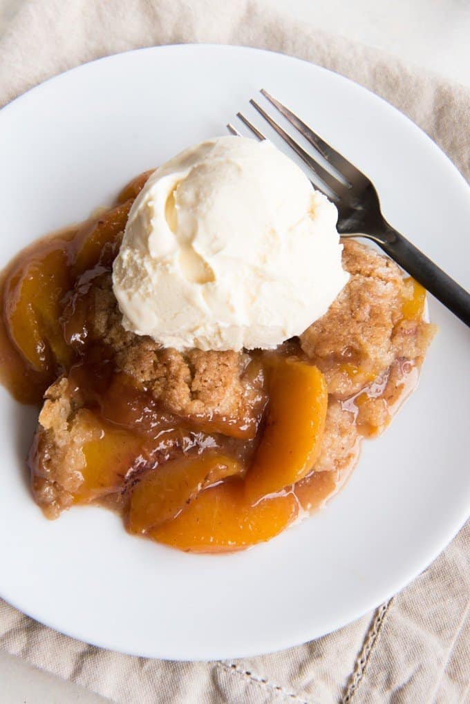 a peach cobbler on a white plate with a scoop of ce cream on top