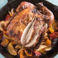 a baked whole chicken in a cast iron skillet with some slices made in the breast