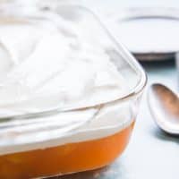 orange jello salad in a baking dish topped with whipped cream