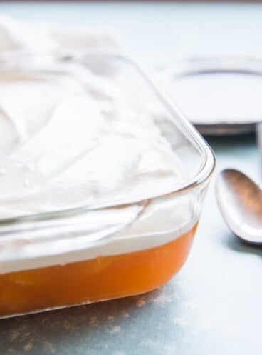orange jello salad in a baking dish topped with whipped cream