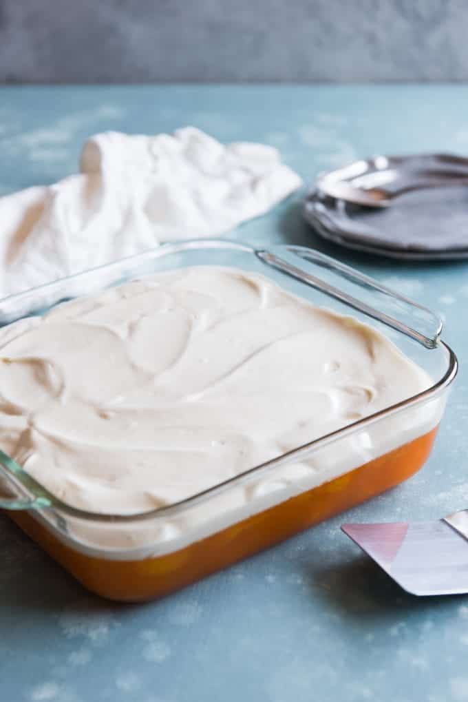whipped cream topped orange jello salad in a baking dish