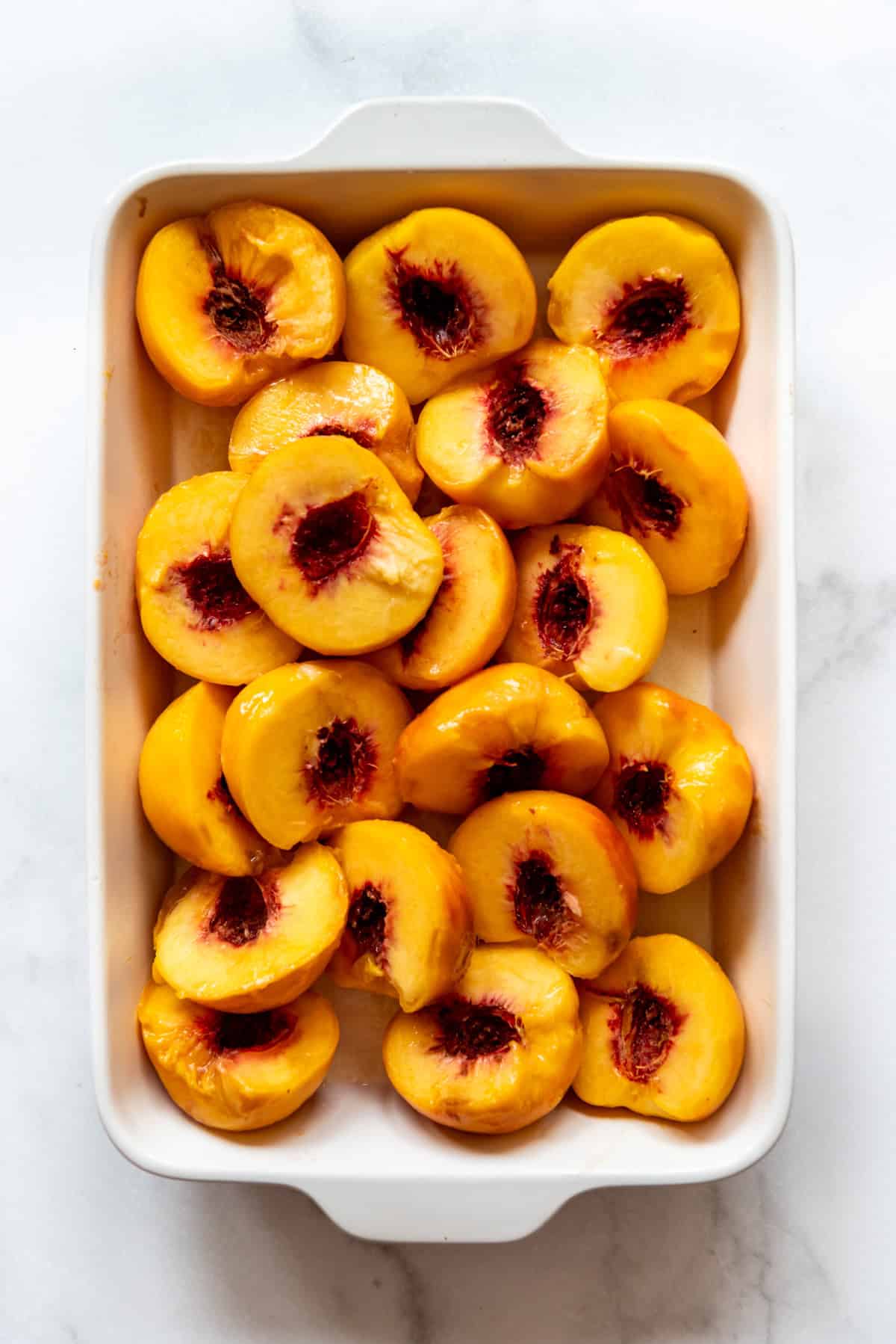 Sliced and peeled peach halves in a white baking dish.