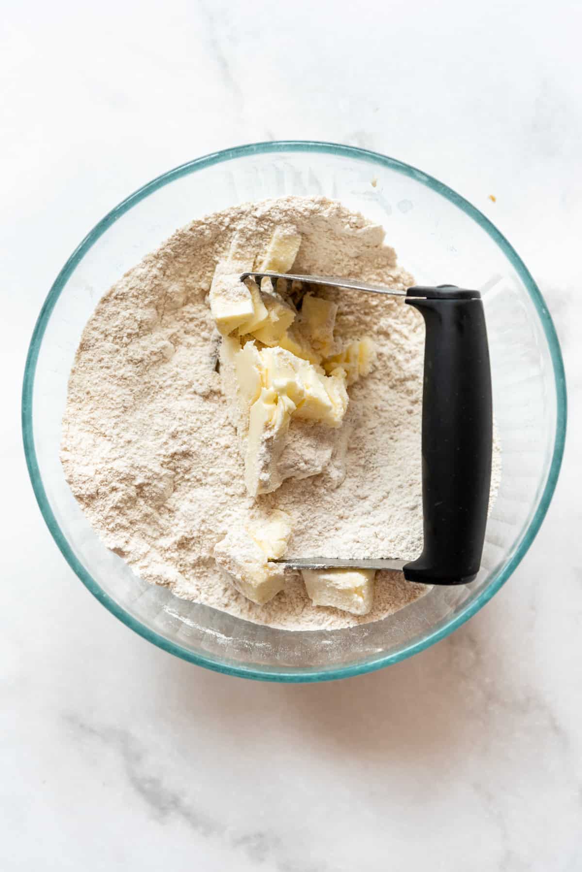 Cutting butter into dry ingredients in a bowl with a pastry cutter.