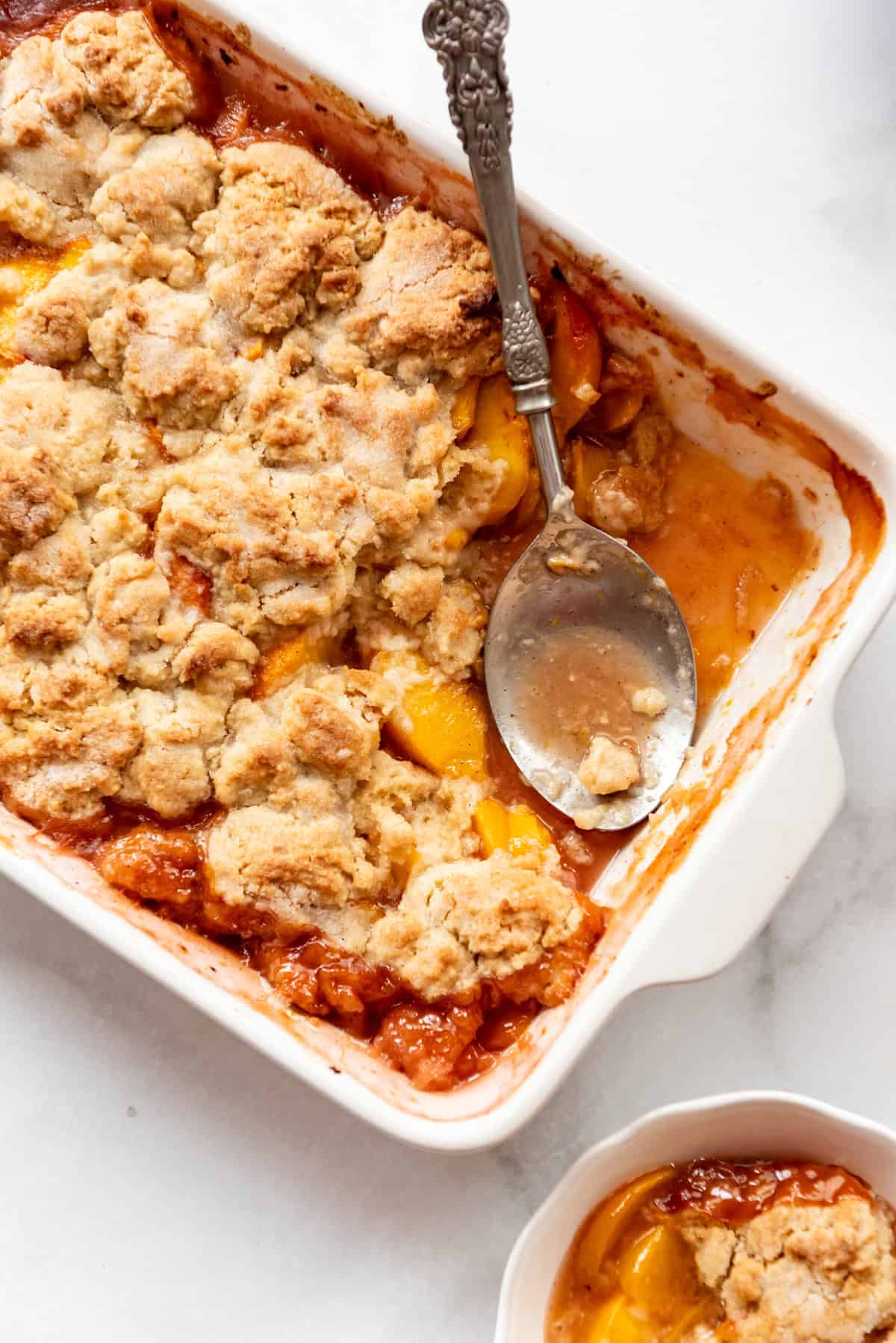 A baking dish of peach cobbler with a serving spoon in it.