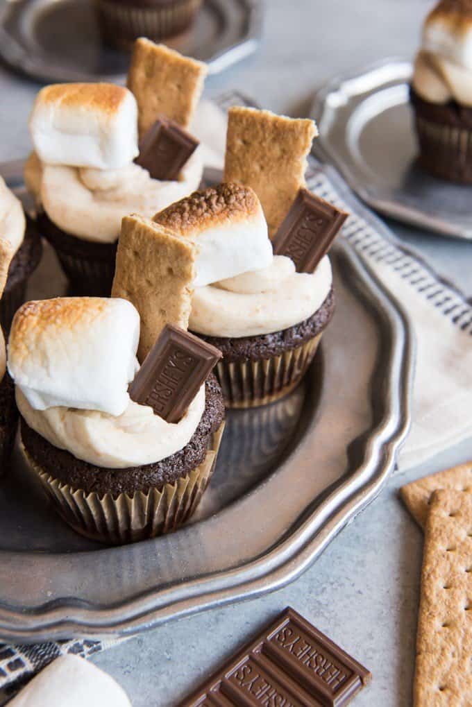 smores cupcakes on a white plate with graham crackers chocolate bars and toasted marshmallows