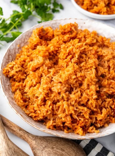 A side view of a bowl full of mexican rice next to wooden spoons.