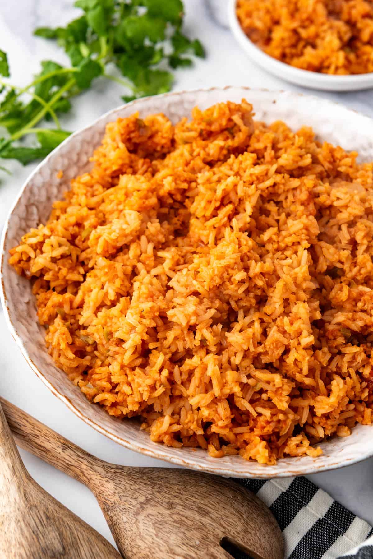 A side view of a bowl full of mexican rice next to wooden spoons.