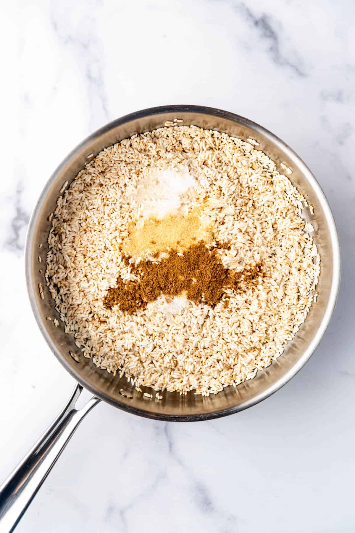 Adding spices to toasted rice in a pan.