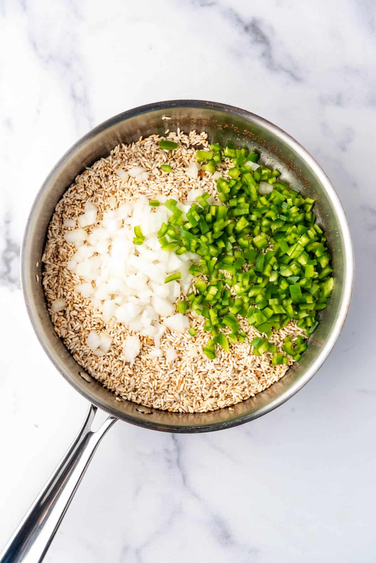 Adding diced onion and pepper to a pan of rice.