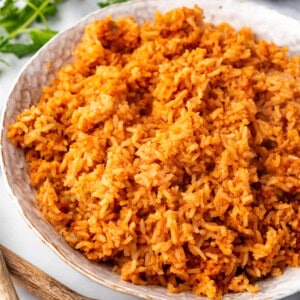 A side view of a bowl full of mexican rice next to wooden spoons.