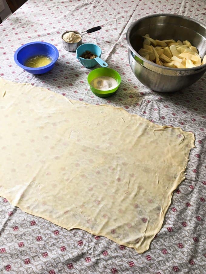 Ingredienti per fare lo streudel tedesco alle mele con una pasta stesa in un rettangolo così sottile che si può vedere il disegno della tovaglia attraverso di esso