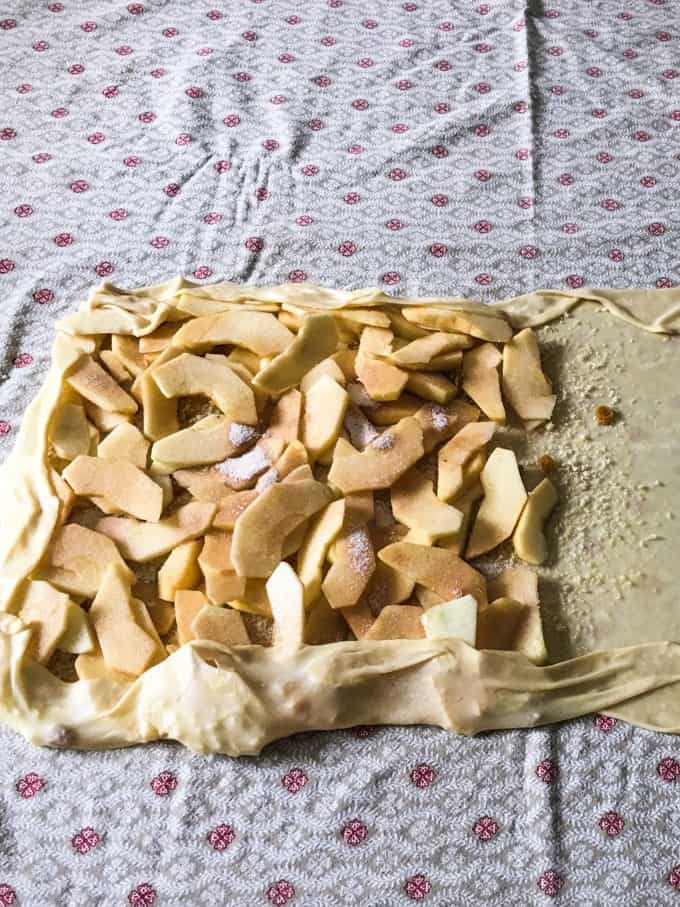 le fette di mela si ammucchiano sul sottile rettangolo di pasta e alcuni dei bordi sono stati tirati su