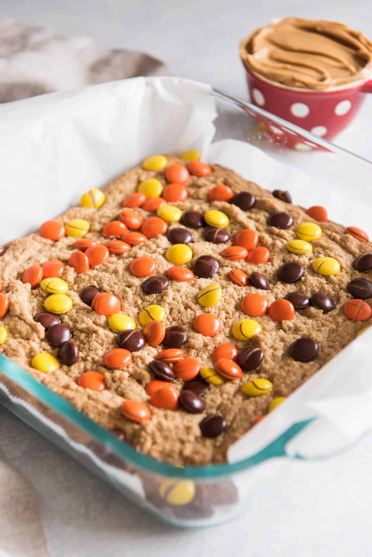 A glass 8x8 baking dish with peanut butter blondies topped with peanut butter Reese's Pieces.