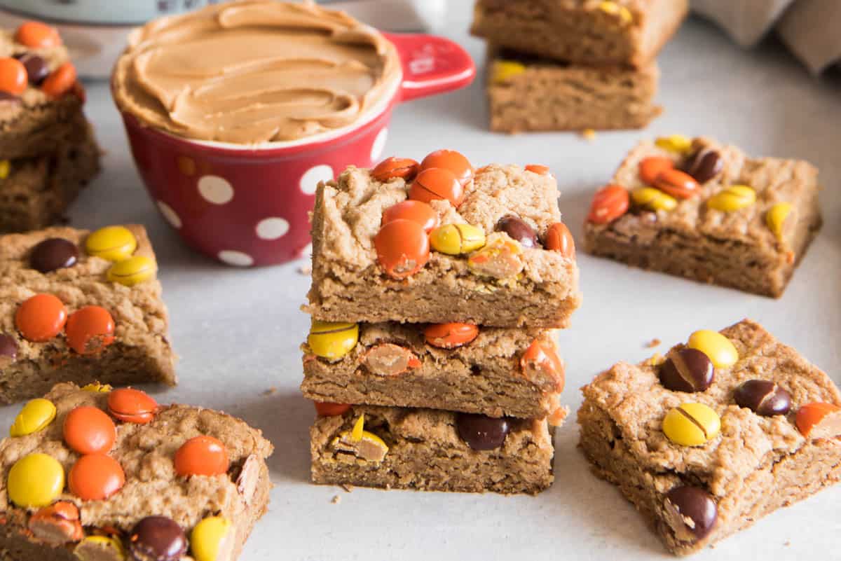 Stacked peanut butter blondies in front of a cup of creamy peanut butter.