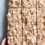 a hand reaching out and grabbing a square of rice krispie