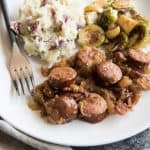 Sauerkraut and Sausages with Apples on a white plate filled with mashed potatoes and brussels sprouts