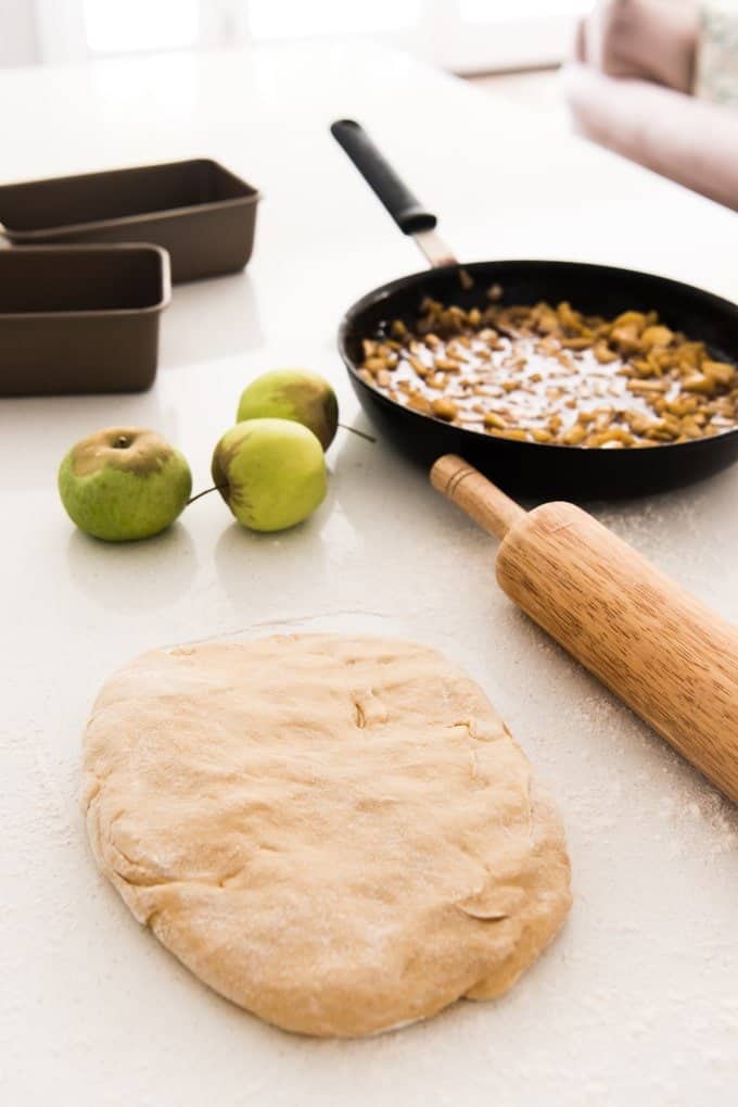 dough on a counter with a rolling pin bread loaf pans skillet and whole apples
