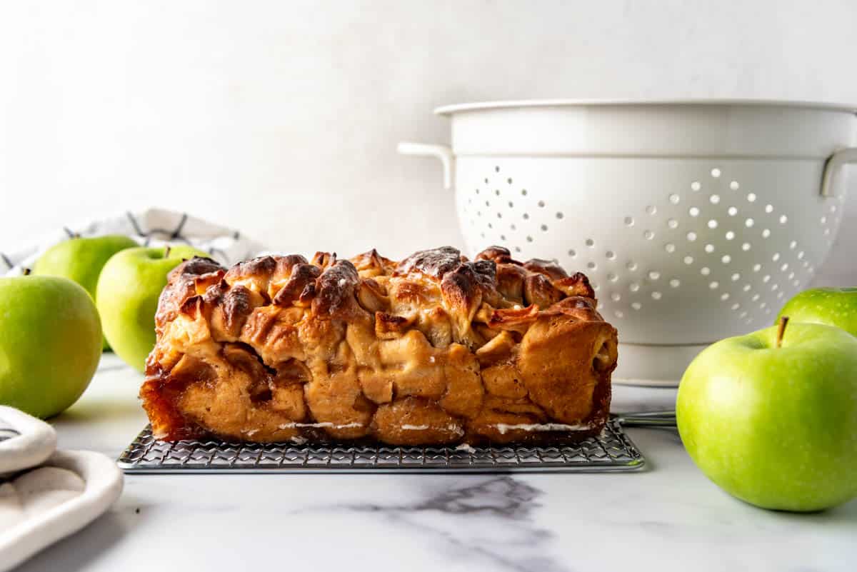 A loaf of apple fritter bread next to Granny Smith apples and a white colander.