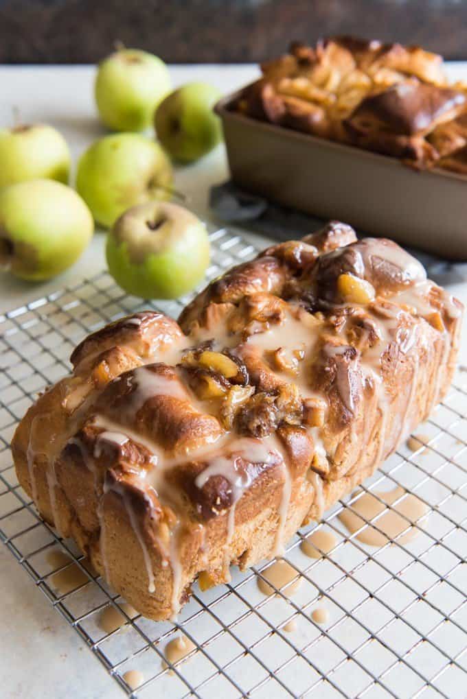 baked apple fritter bread on a wire rack whole apples and other loaf in background