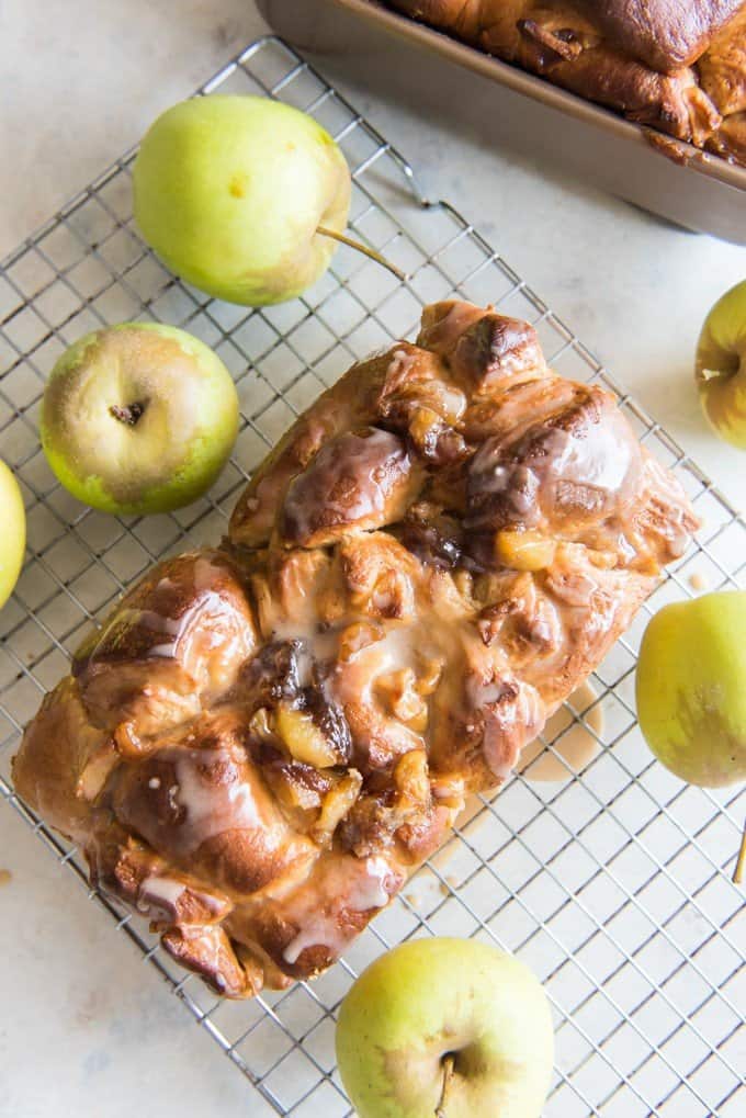 an aerial view of glazed apple fritter bread on wire rack withwhole apples around it