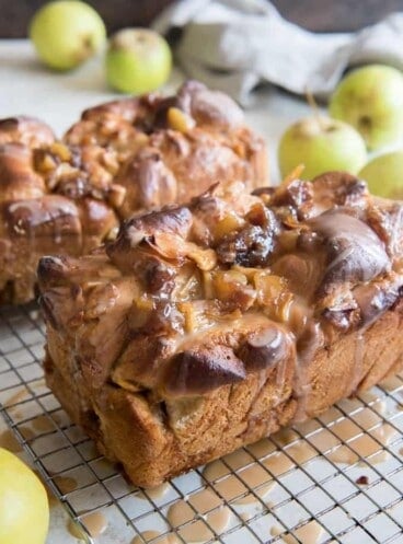 loaves of apple fritter yeast bread on wire racks surrounded by green apples