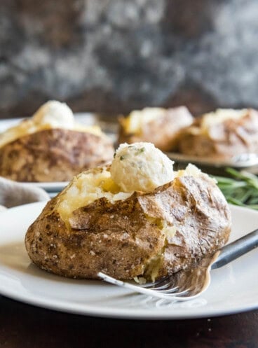 Baked potatoes on plates with scooped balls of butter on top.