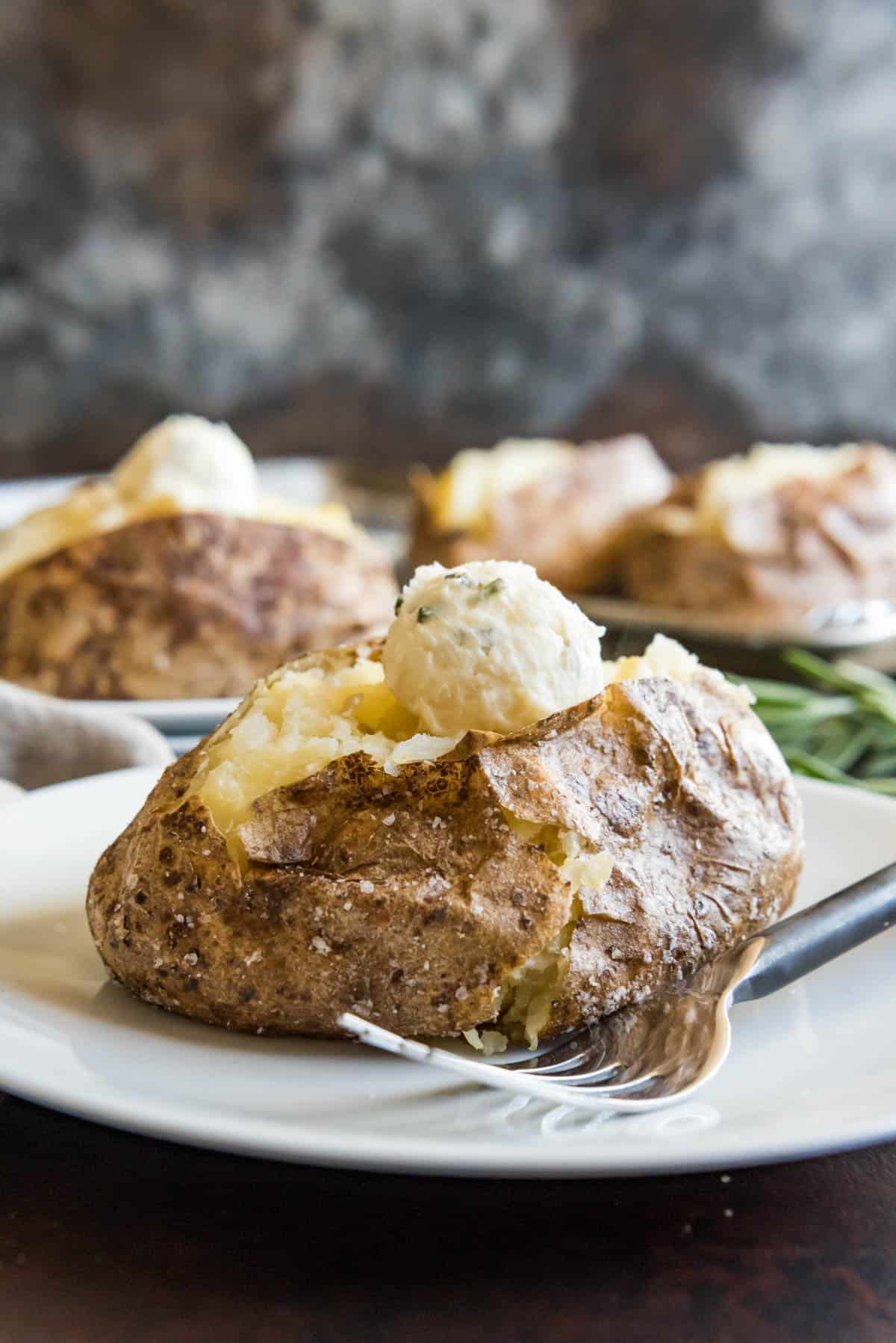 Baked potatoes on plates with scooped balls of butter on top.