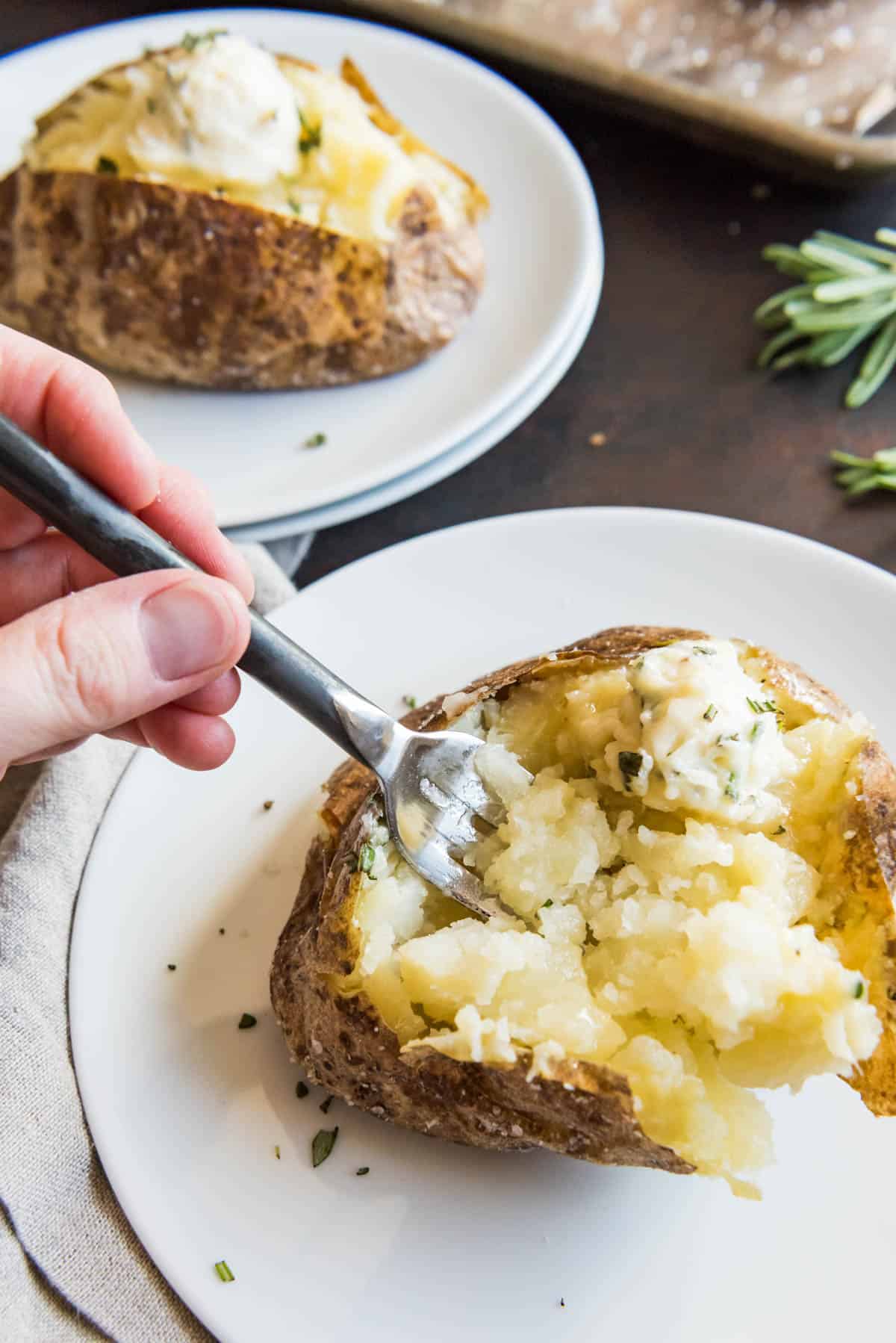 Hand holding a fork digging into a fluffy salt crusted baked potato side dish.